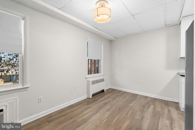 empty room featuring a drop ceiling, radiator, and light wood-type flooring