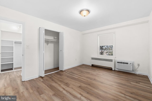 unfurnished bedroom with radiator, a wall mounted air conditioner, light hardwood / wood-style flooring, and a closet