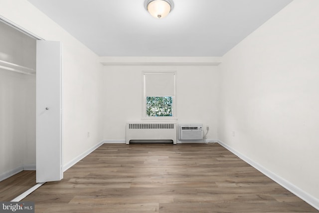 unfurnished bedroom featuring light hardwood / wood-style floors, radiator, a wall unit AC, and a closet