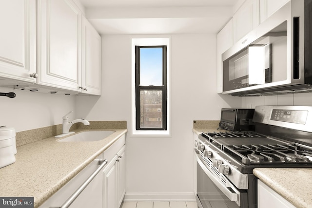 kitchen with sink, white cabinetry, light tile patterned floors, stainless steel appliances, and light stone countertops