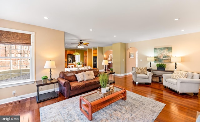 living area with arched walkways, recessed lighting, wood-type flooring, visible vents, and baseboards