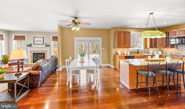 kitchen featuring black microwave, hardwood / wood-style flooring, tasteful backsplash, a kitchen bar, and glass insert cabinets