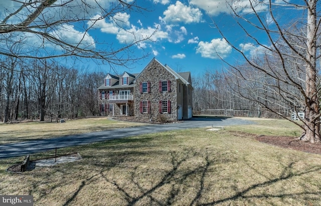 view of front of house featuring stone siding, a front lawn, a balcony, and driveway