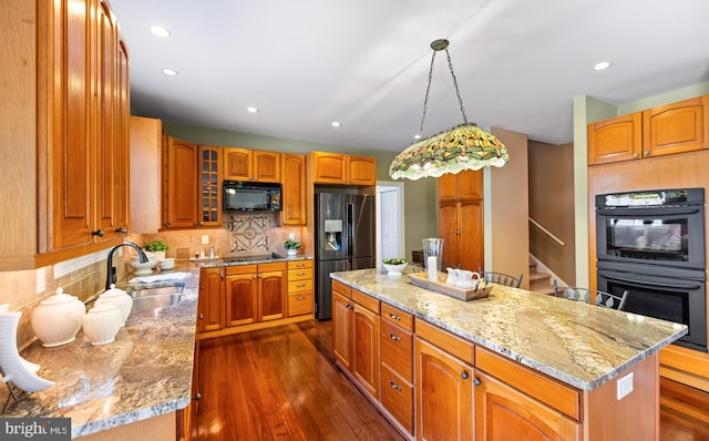 kitchen with a kitchen island, a sink, light stone counters, and black appliances