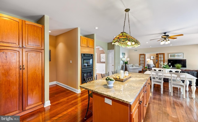 kitchen with dobule oven black, a breakfast bar, open floor plan, light stone countertops, and a glass covered fireplace