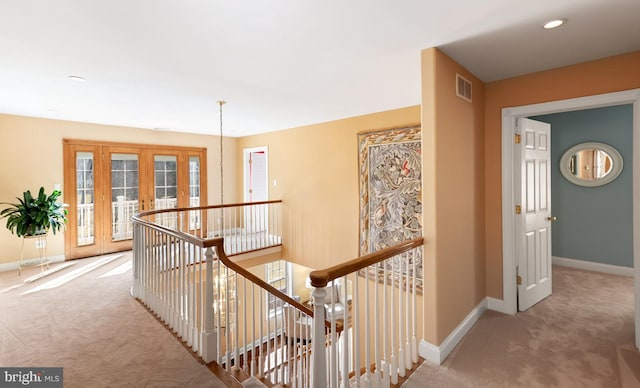 hall featuring carpet, visible vents, baseboards, and an upstairs landing