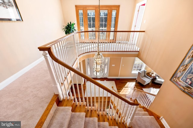 stairs featuring a high ceiling, an inviting chandelier, carpet flooring, wood finished floors, and baseboards