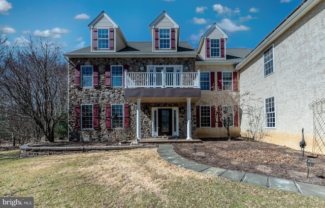 georgian-style home with a balcony, stone siding, and a front yard