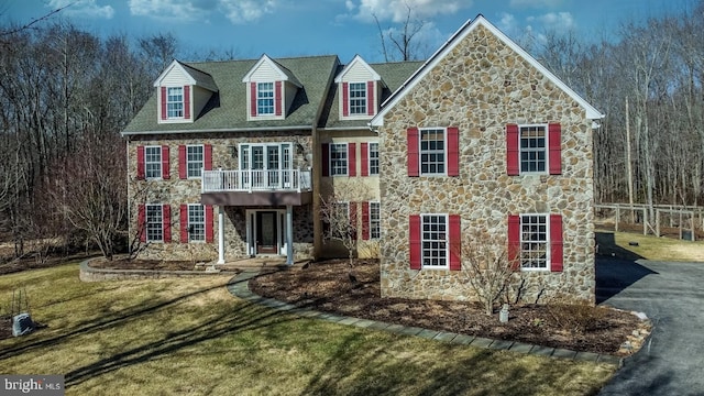 georgian-style home with driveway, stone siding, and a front lawn