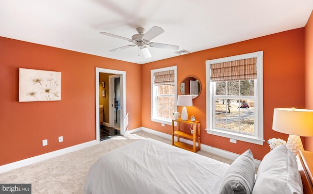 carpeted bedroom featuring a ceiling fan, visible vents, ensuite bath, and baseboards