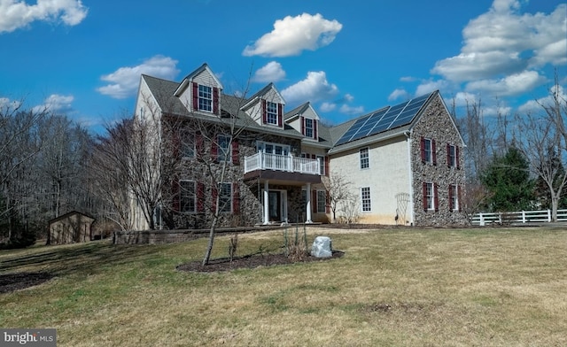 view of front of property featuring a balcony, roof mounted solar panels, fence, and a front yard