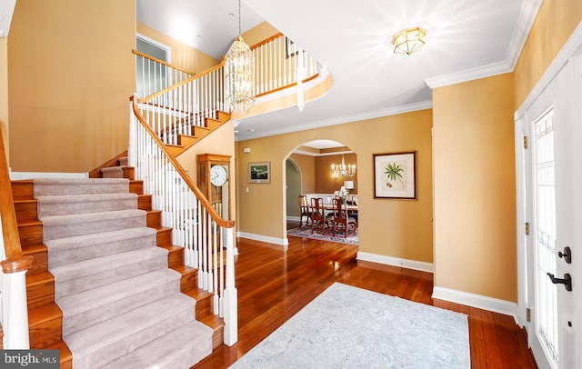 foyer with arched walkways, ornamental molding, a chandelier, baseboards, and hardwood / wood-style flooring