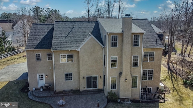 back of house with a chimney, stucco siding, a shingled roof, a patio area, and fence