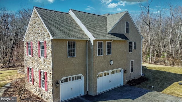 view of side of home with an attached garage, a shingled roof, a yard, driveway, and stucco siding