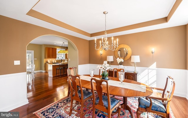 dining area featuring a tray ceiling, a wainscoted wall, and arched walkways