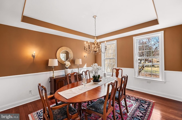 dining area with a raised ceiling, a wainscoted wall, wood-type flooring, and an inviting chandelier