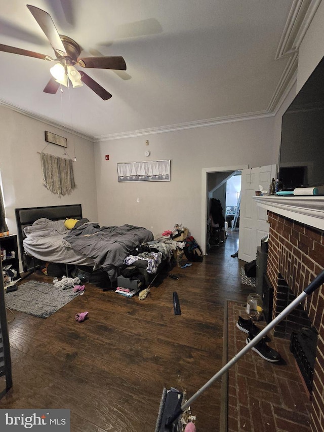 bedroom with a brick fireplace, crown molding, dark wood-type flooring, and ceiling fan