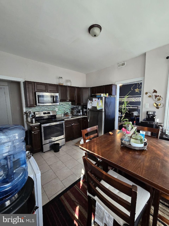 kitchen featuring sink, backsplash, light tile patterned floors, dark brown cabinetry, and stainless steel appliances