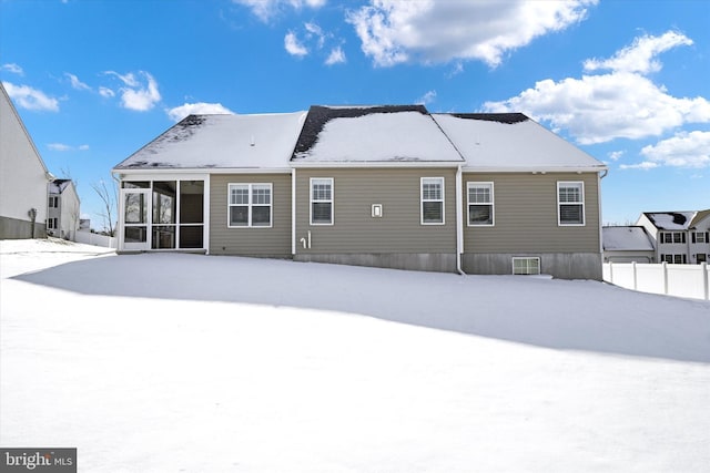 snow covered back of property featuring a sunroom