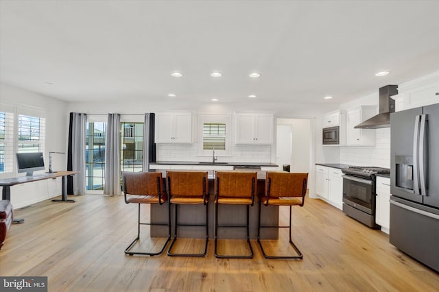 kitchen with a kitchen island, appliances with stainless steel finishes, sink, white cabinets, and wall chimney range hood