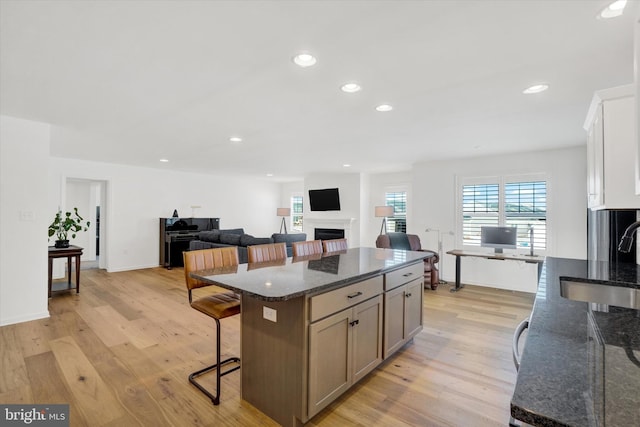 kitchen with sink, light hardwood / wood-style flooring, a breakfast bar area, white cabinetry, and dark stone counters