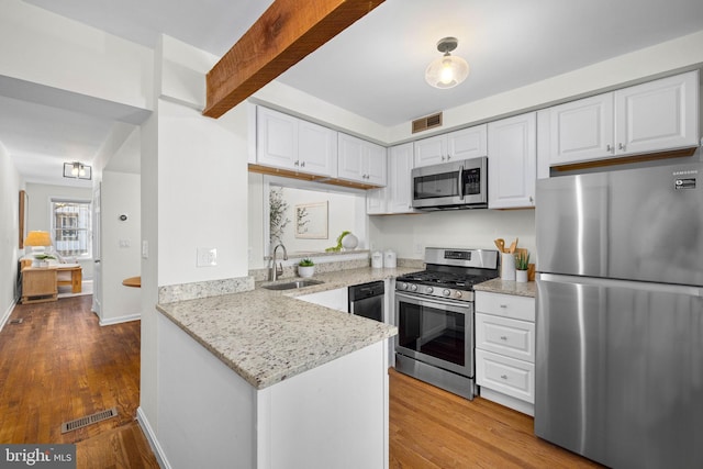 kitchen with beamed ceiling, sink, white cabinets, light stone counters, and stainless steel appliances