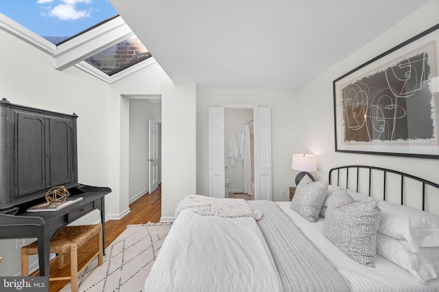 bedroom with hardwood / wood-style floors, vaulted ceiling with skylight, and ensuite bathroom