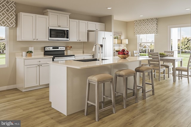 kitchen featuring stainless steel range with electric stovetop, built in microwave, an island with sink, and white cabinets