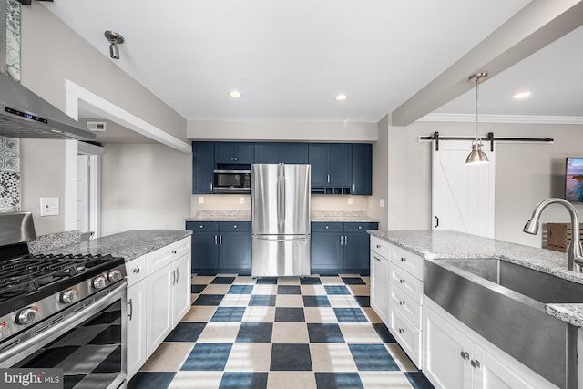 kitchen featuring wall chimney exhaust hood, blue cabinets, stainless steel appliances, a barn door, and white cabinets