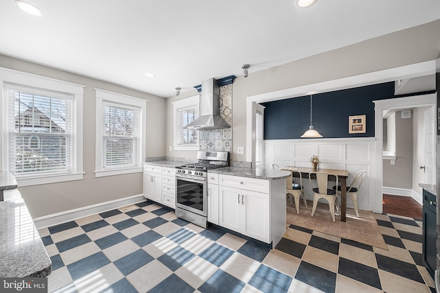 kitchen featuring stone counters, pendant lighting, white cabinets, gas stove, and wall chimney range hood