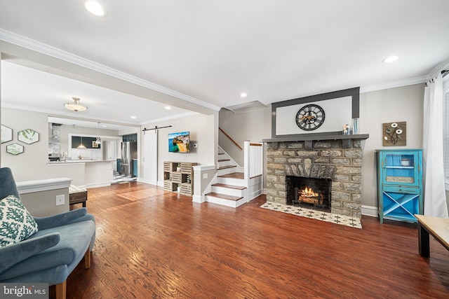 living room featuring ornamental molding, a barn door, wood-type flooring, and a fireplace