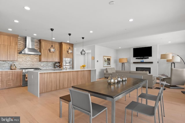 kitchen with pendant lighting, appliances with stainless steel finishes, decorative backsplash, wall chimney exhaust hood, and light wood-type flooring