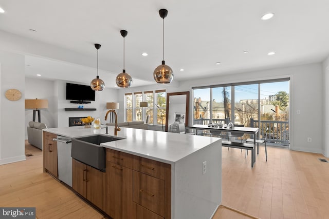 kitchen with stainless steel dishwasher, sink, a center island with sink, and light hardwood / wood-style flooring