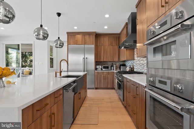 kitchen with hanging light fixtures, tasteful backsplash, premium appliances, wall chimney exhaust hood, and light wood-type flooring