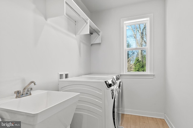 clothes washing area featuring sink, washing machine and clothes dryer, and light hardwood / wood-style flooring