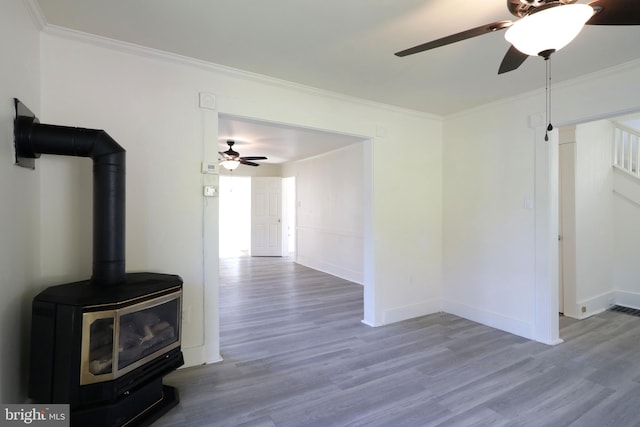 unfurnished living room with ornamental molding, a wood stove, light wood-style flooring, and baseboards