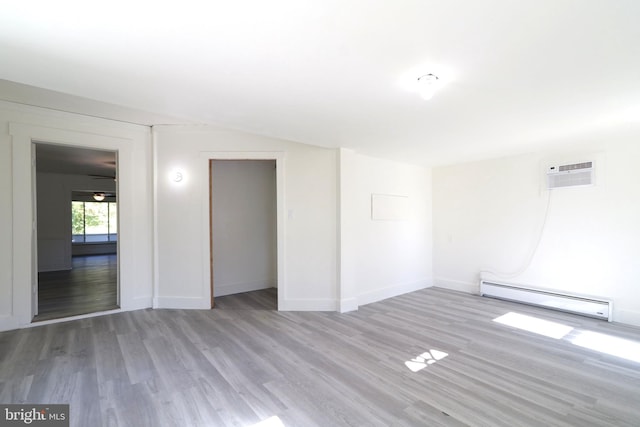 spare room featuring light wood finished floors, baseboards, lofted ceiling, baseboard heating, and an AC wall unit