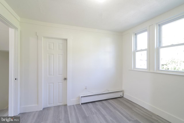 spare room featuring baseboards, baseboard heating, and light wood-style floors