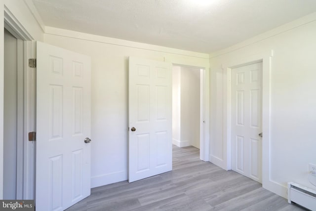 unfurnished bedroom featuring light wood-type flooring, a baseboard radiator, baseboards, and a textured ceiling