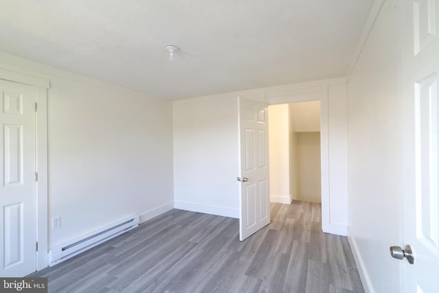 spare room featuring a baseboard heating unit, baseboards, and wood finished floors