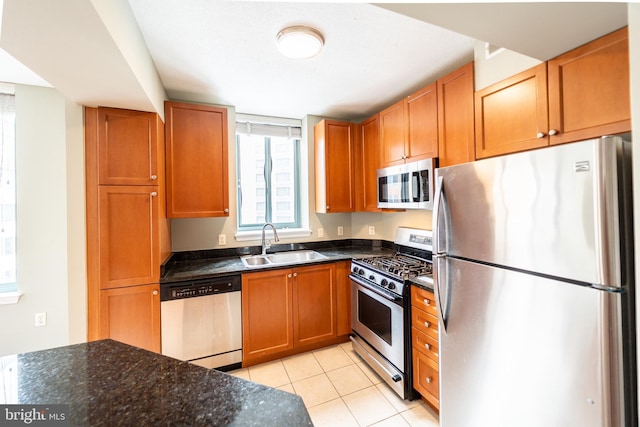 kitchen with sink, stainless steel appliances, dark stone countertops, and light tile patterned floors