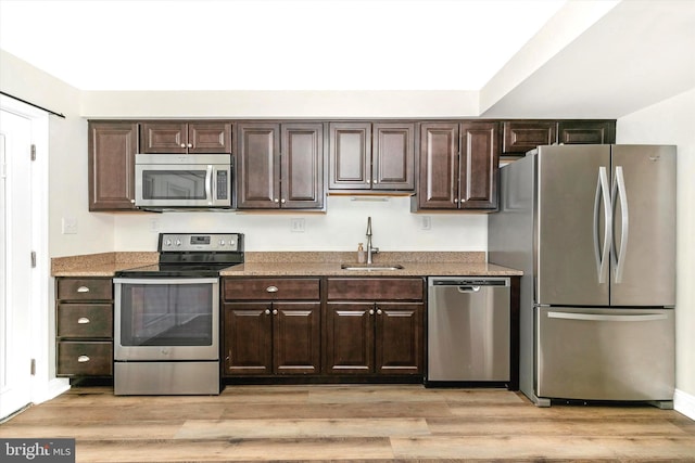 kitchen with light wood finished floors, appliances with stainless steel finishes, dark brown cabinets, and a sink