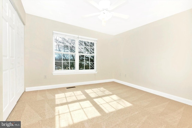 carpeted spare room featuring visible vents, a ceiling fan, and baseboards