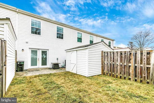 back of house featuring a lawn, an outbuilding, fence, a storage unit, and french doors