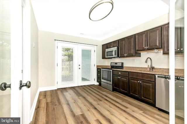 kitchen with dark brown cabinetry, stainless steel appliances, french doors, light wood-style floors, and a sink