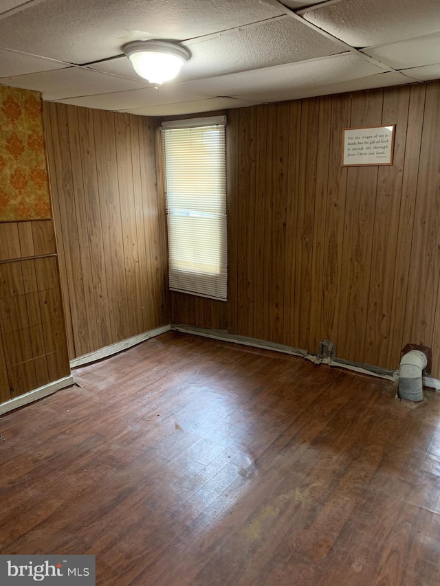 empty room with a drop ceiling, hardwood / wood-style flooring, and wooden walls