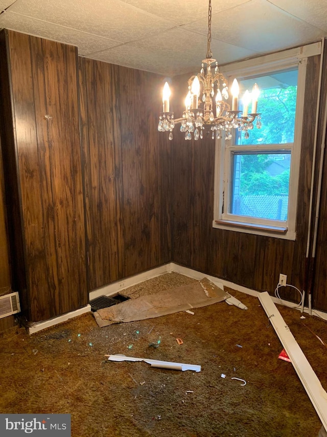 unfurnished dining area featuring an inviting chandelier and wood walls