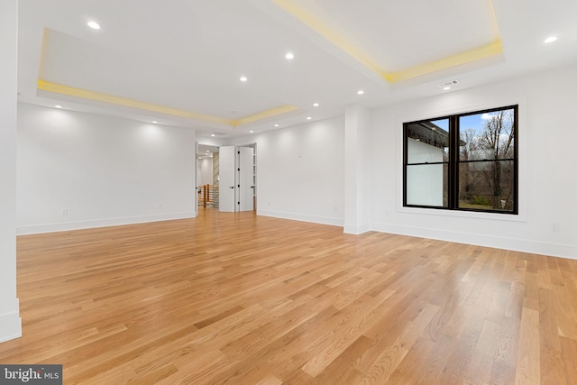 spare room with a tray ceiling and light hardwood / wood-style floors