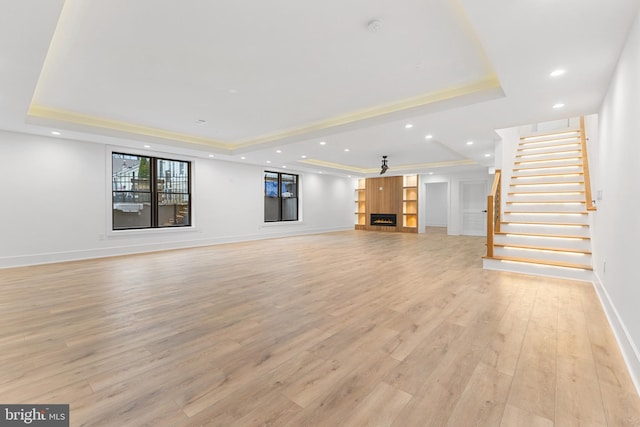 unfurnished living room featuring a raised ceiling and light wood-type flooring