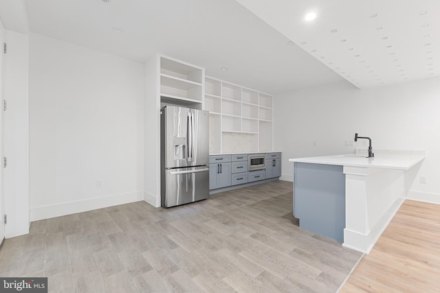 kitchen featuring gray cabinets, stainless steel appliances, kitchen peninsula, and light wood-type flooring